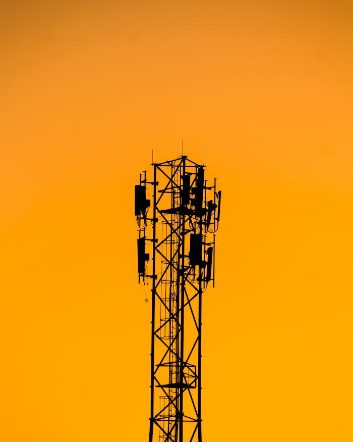 A telecommunication tower silhouetted against a vibrant orange sunset sky in India.