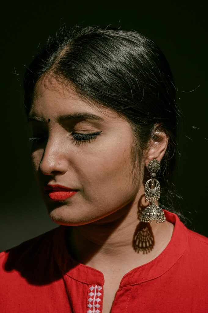 A serene portrait of a woman with eyes closed, wearing silver earrings and red attire.